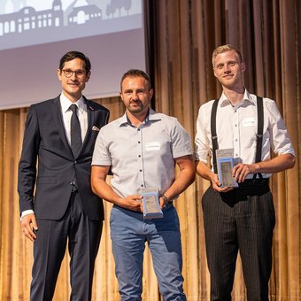 Felix Manzke, Präsident des Bundesverbandes Transportbeton steht mit zwei Absolventen der IHK-Industriemeister-Weiterbildung auf einer Bühne. 