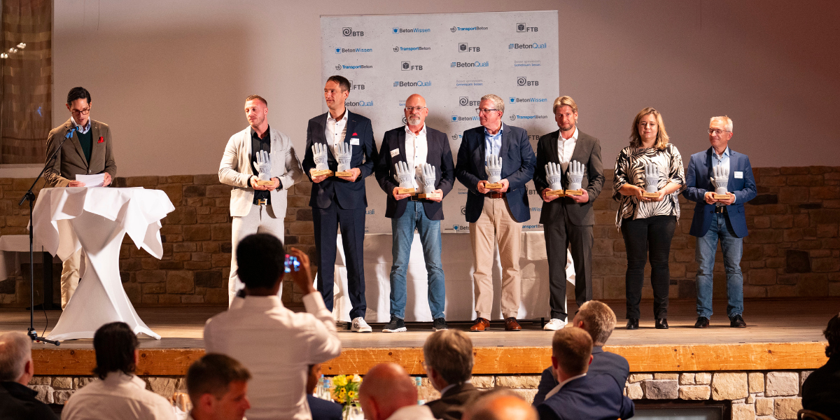 BTB-Präsident Felix Manzke mit den Vertreterinnen und Vertretern der ausgezeichneten Unternhemen. Diese halten auf einer Bühne stehend die Pokale aus Beton in Form eines Arbeitshandschuhs in der Hand.