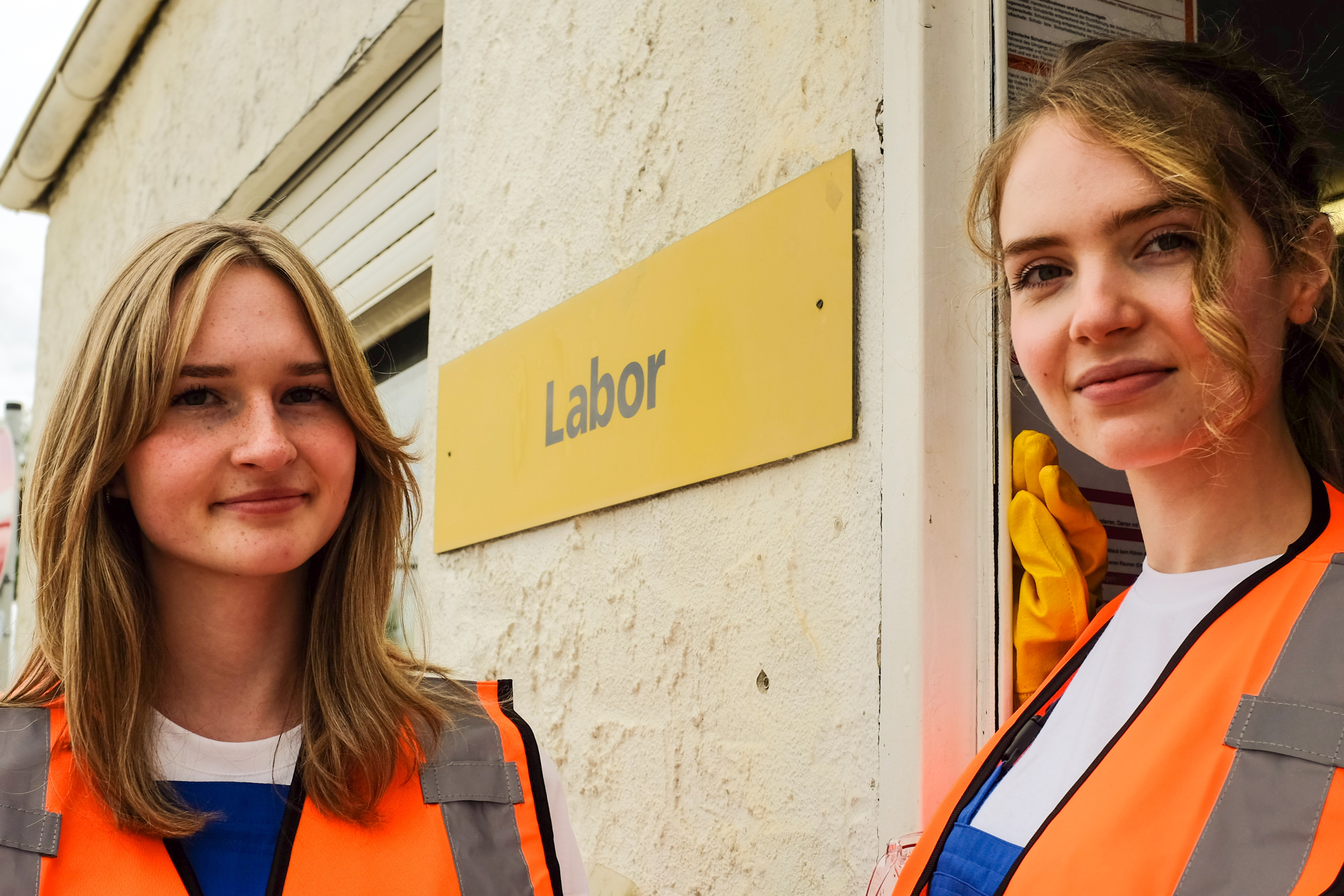 Twei Auszubildende stehen vor einem Schild mit der Ausfschrift „Labor" an einem Gebäude