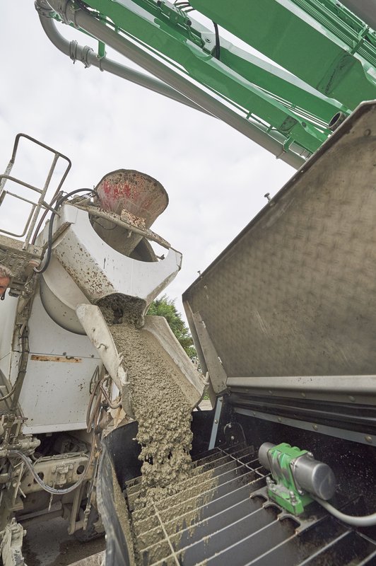 Frischer Beton, auf der Rutsche eines Fahrmischers zur Übergabe an eine Betonpumpe