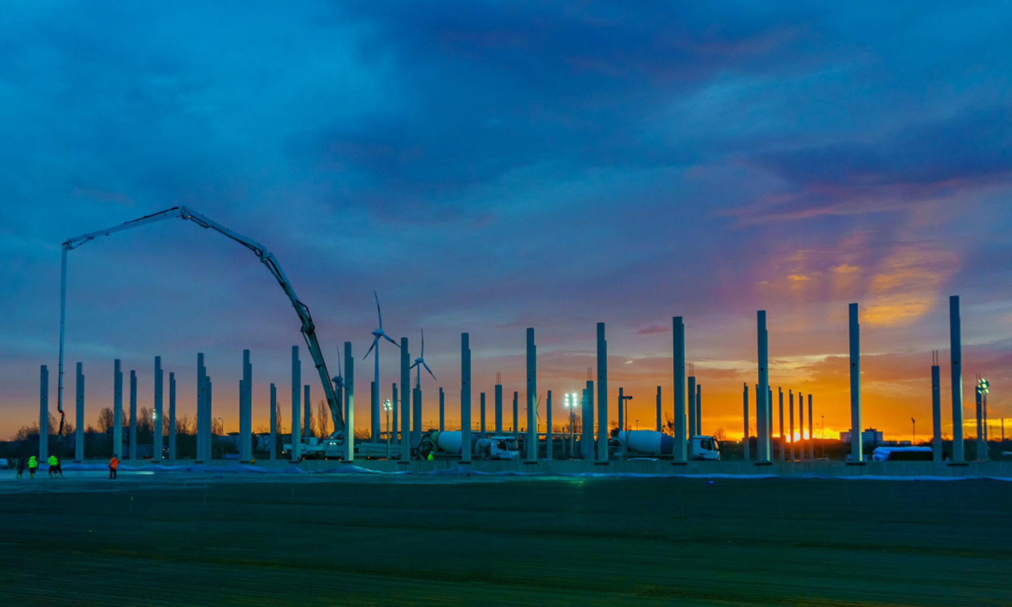 Ein Fundament wird in einer Abendstimmung benoniert. Zu sehen sind Arbeitspersonen, einige Fahrmischer und eine Betonpumpe